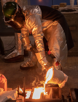A student wearing full safety gear while pouring liquid metal in the foundry